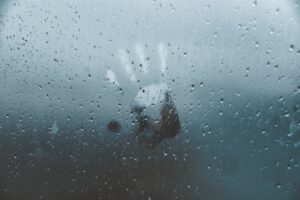 A handprint on a foggy, rain-covered glass window.